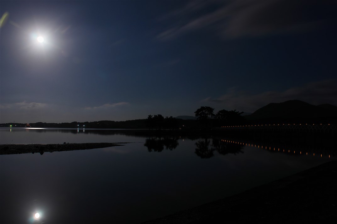 夜の水面の奥に見える大陸と月の写真