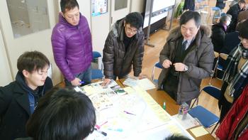 机に広げられた資料を基に話し合う男性たちの写真