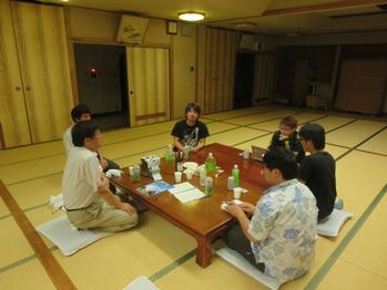 畳の広間の中で、四角いちゃぶ台を囲んで打ち合わせをしている6人の大人の写真