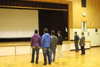 体育館のステージを注視している6人の男性の写真