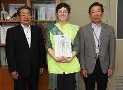 賞状を持った女性の両隣に男性が立っている写真