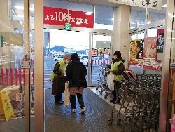 店の風除室にて女性が女性買い物客に啓発物品を渡している写真