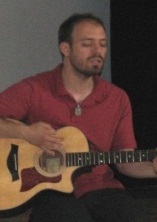 目を瞑ってギターを弾いている男性の写真