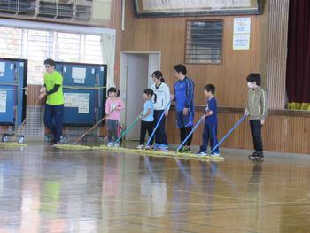 大人4人と子ども3人がモップを手に、一列に並んで体育館の床を掃除している写真