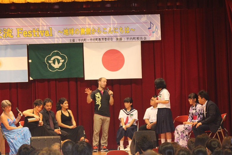 アルゼンチン国旗・平内町のシンボル・日本の国旗が掛けられた壇上でマイクを持って対話をしている女子生徒と外国人の写真