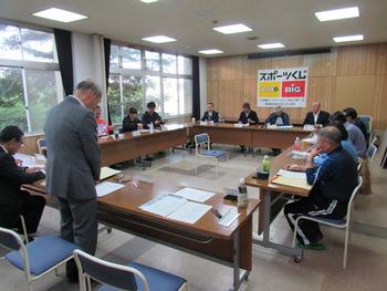 会議室で長方形に並べた長机の椅子に座り、スーツを着た人たちが会議している写真