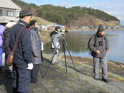 水辺に向けて構えている三脚カメラの周りに人が集まっている写真