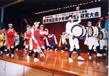 壇上で赤い衣装の人たちと、白い衣装に太鼓を持った人たちが踊っている写真