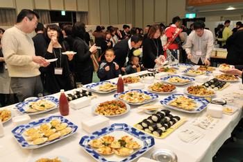 大きなテーブルの上にたくさんの料理が並び、会食をしている人たちの写真