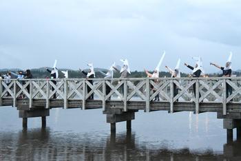 橋の上で、動物と鳥の形をした白い被り物を被った人たちが手を挙げている写真