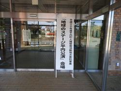 建物の入口に「地球のステージ平内公演会場」と書かれた看板が立てかけられている写真