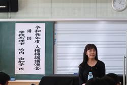 講師の名前が書かれた紙が貼られた黒板の前に女性が立っている写真